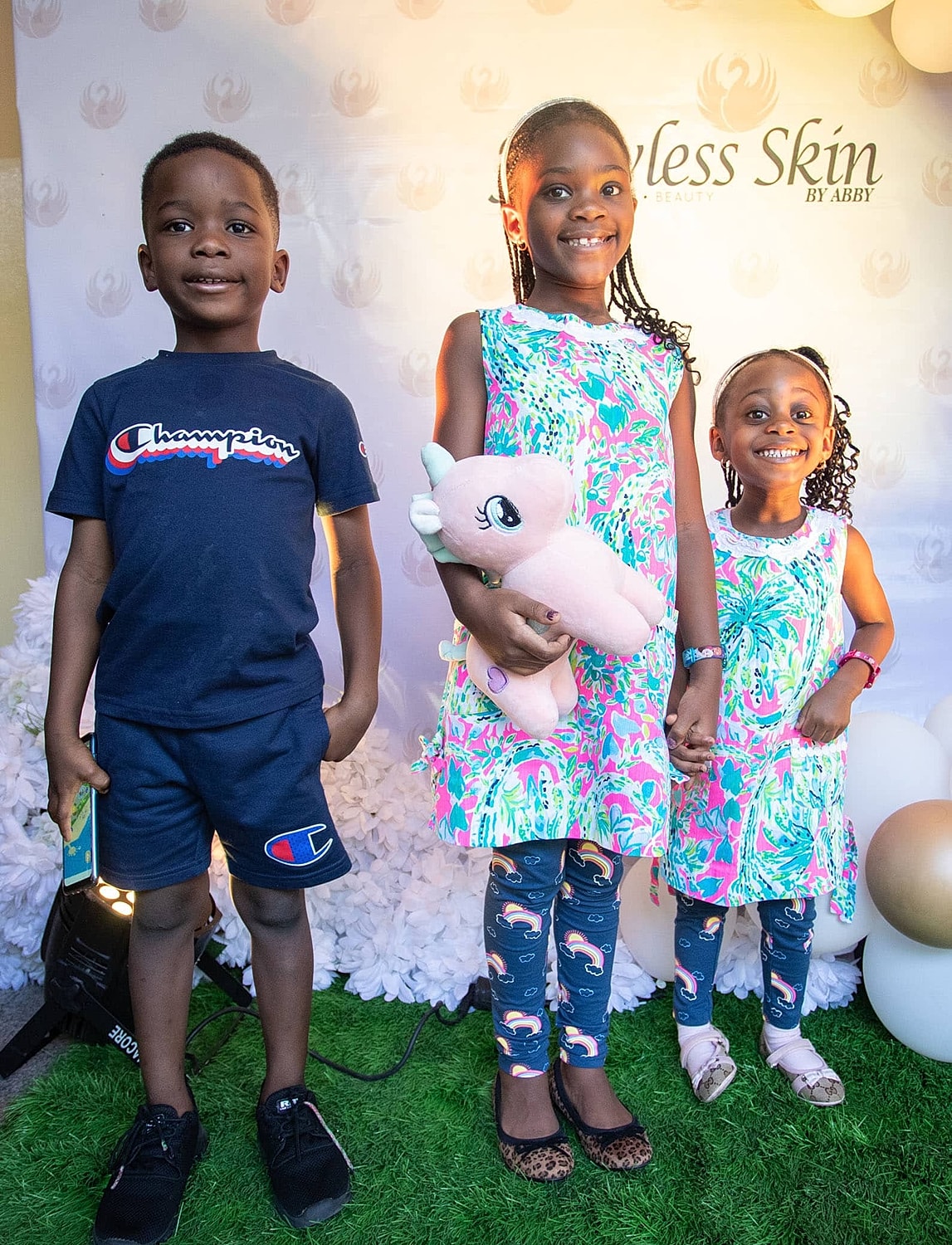 Three kids posing with a stuffed unicorn toy.