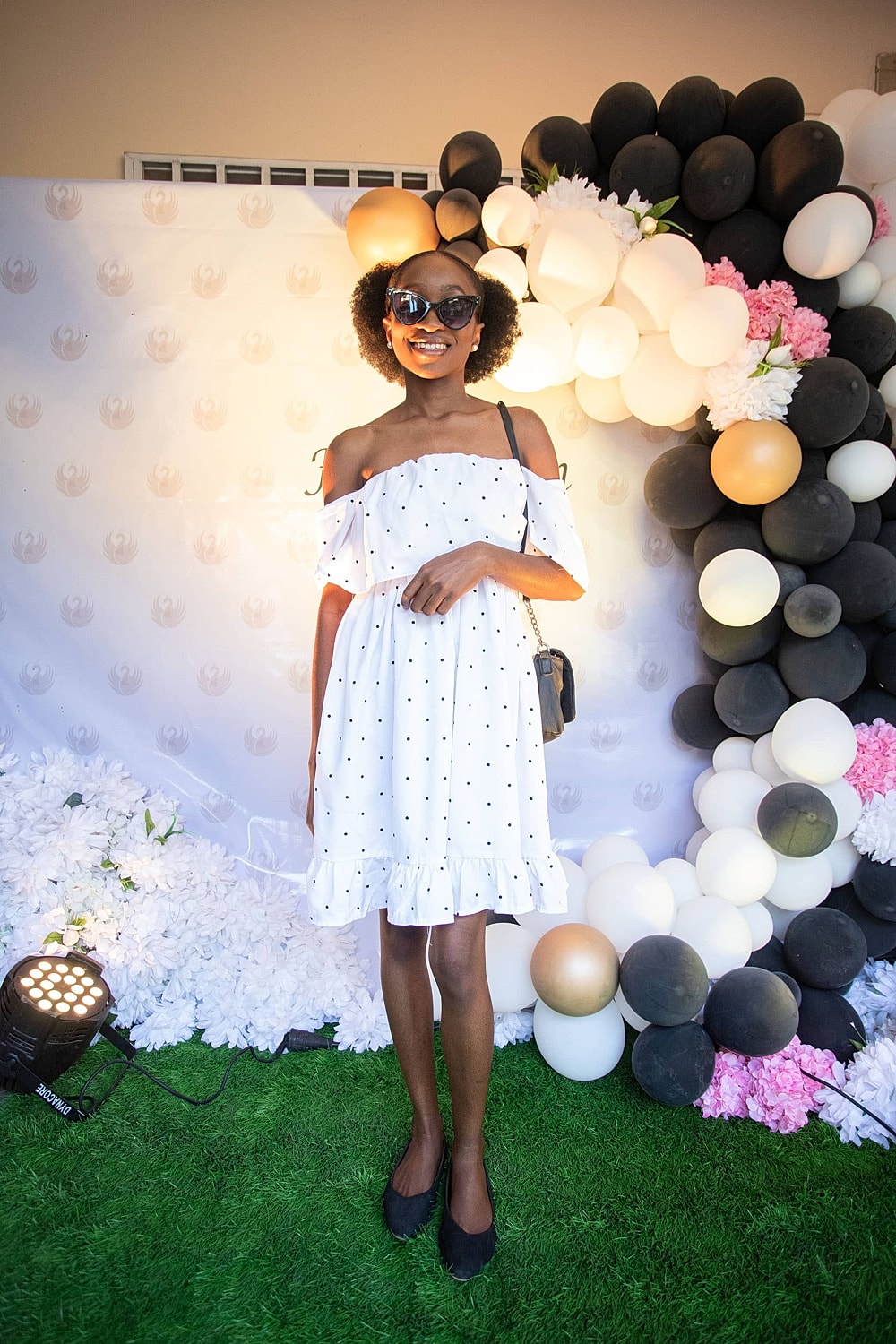 Person in polka dot dress posing by balloons.