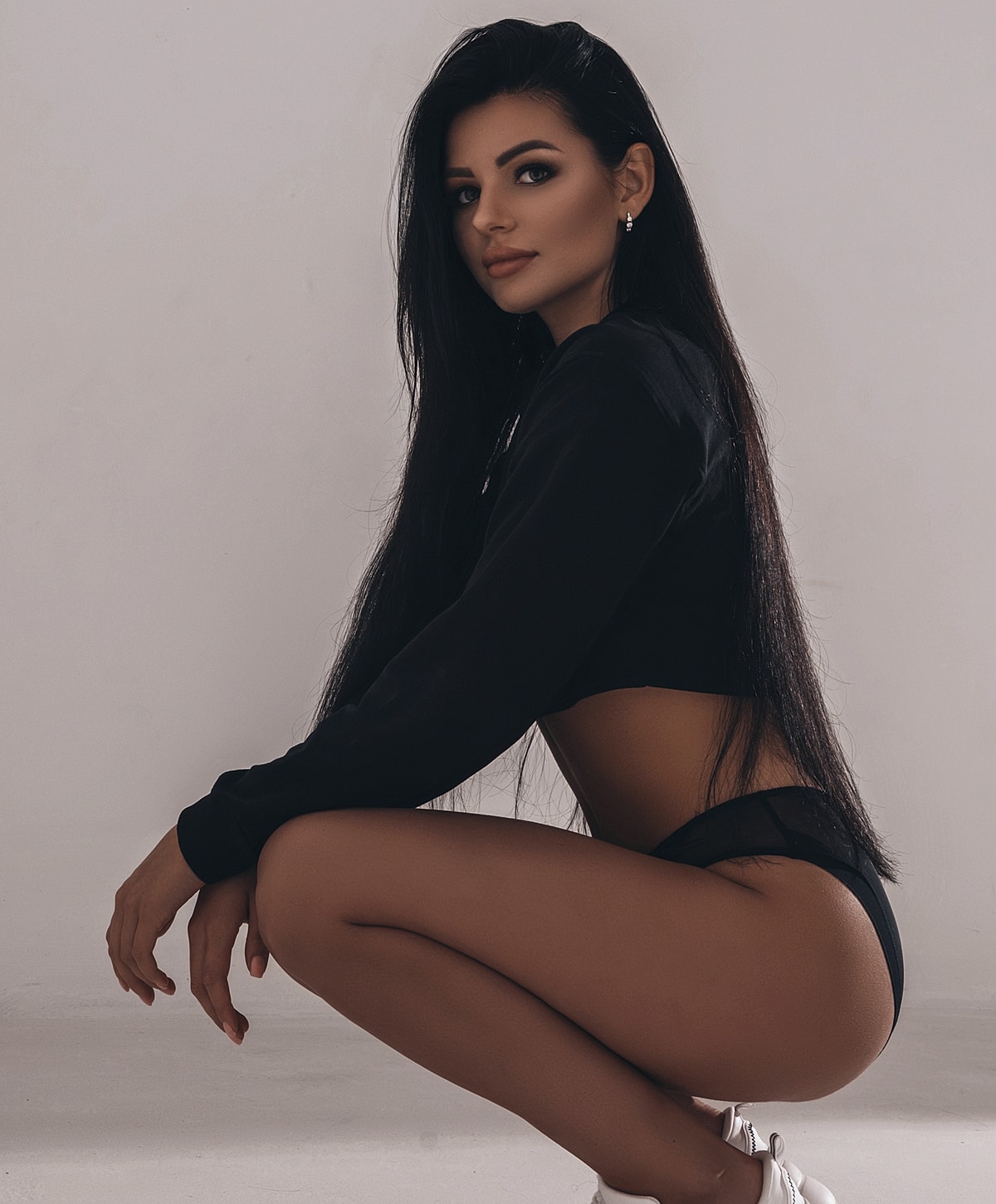 Woman squatting in stylish black outfit, side profile.
