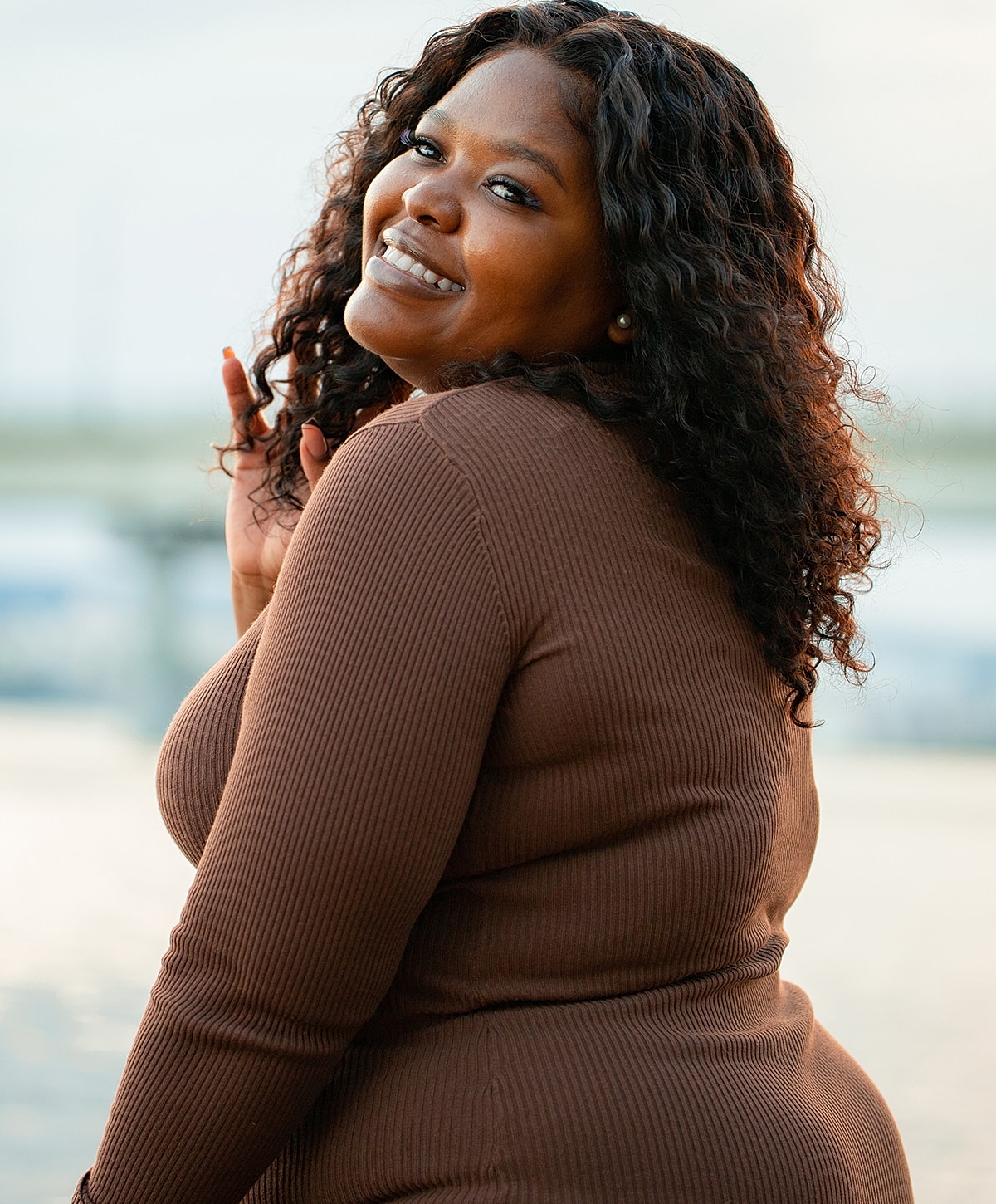 Smiling woman with curly hair outdoors at sunset.