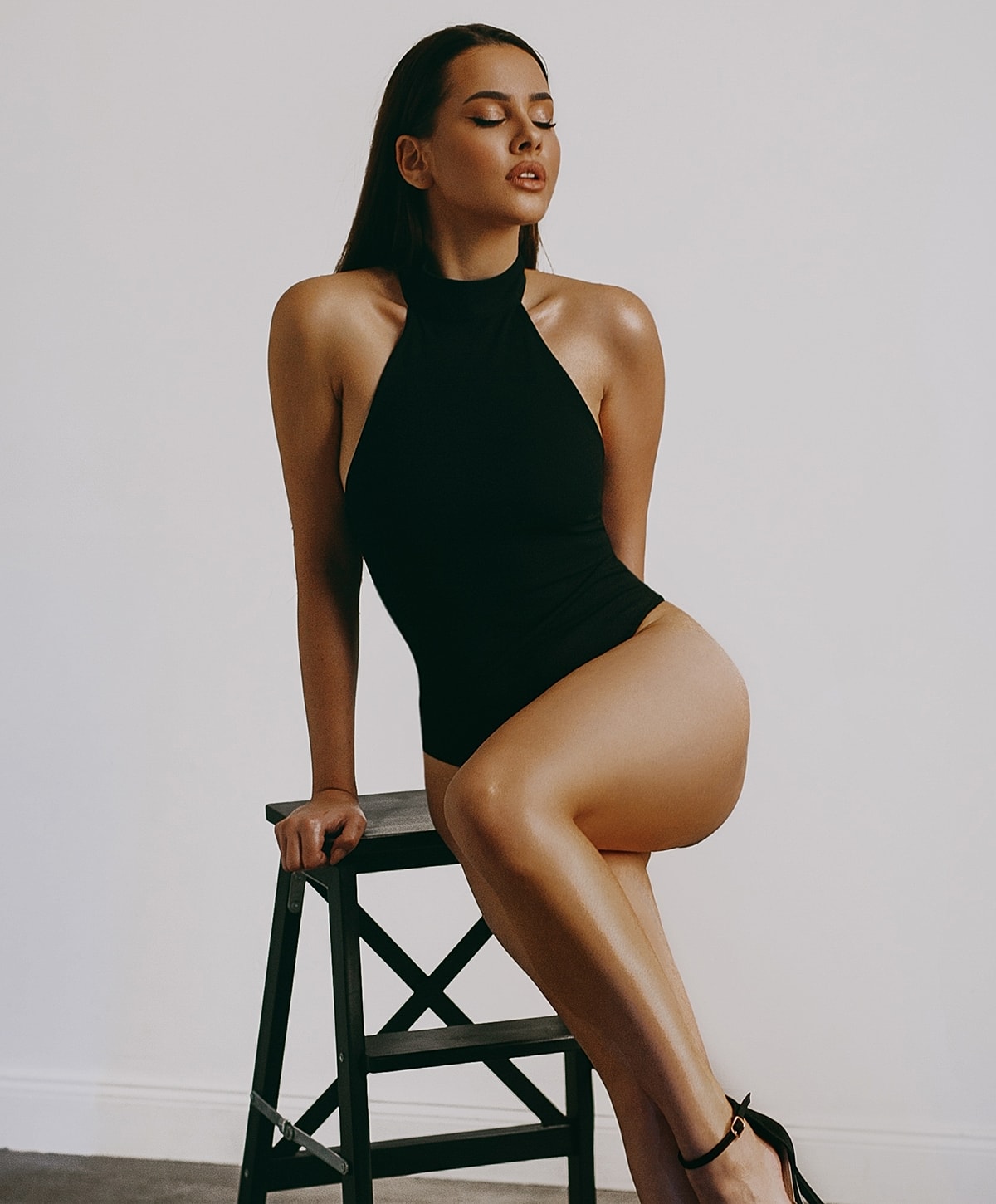 Abuja Liposculpture model seated on stool in stylish black outfit.