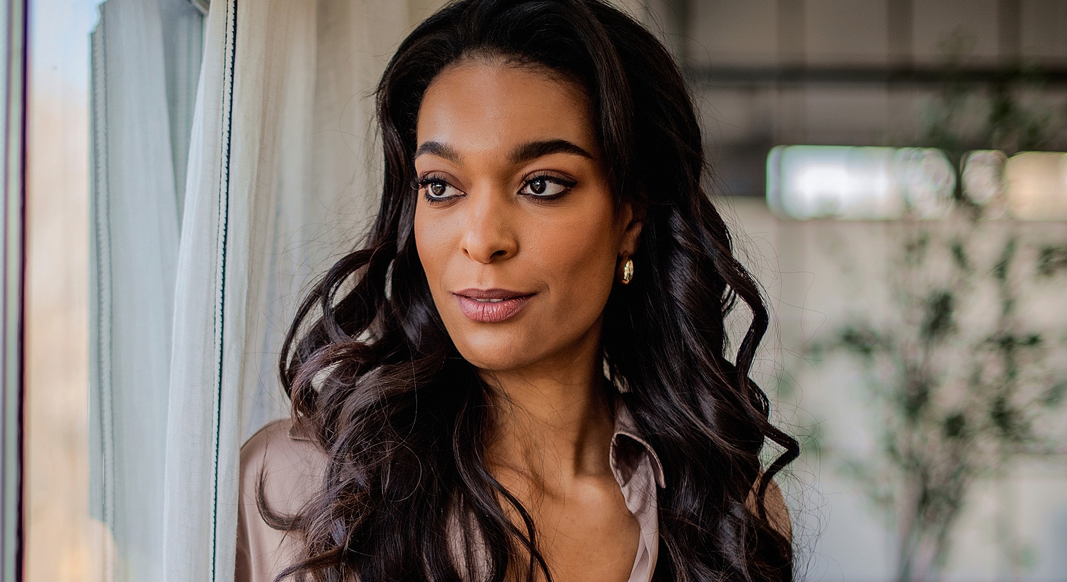 Abuja Brow Lift model with long, curly hair by window.