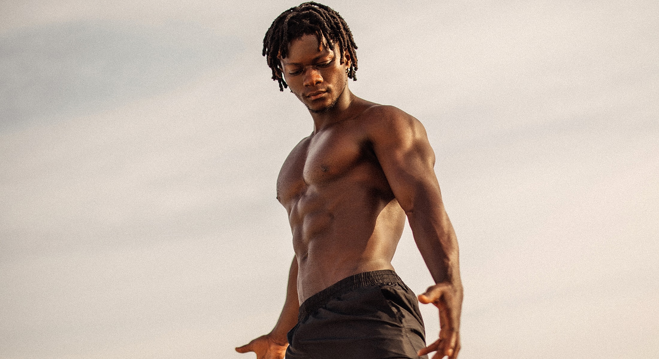 Muscular man posing against a cloudy background.